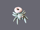 Graue 3D-gedruckte Spinne mit rosa Donut auf dem Rücken